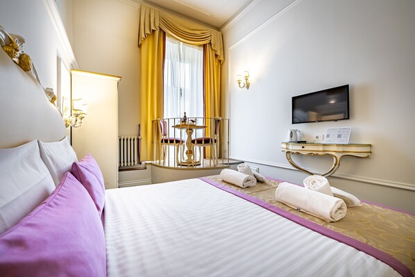 Een hotelkamer met een bed, een klein tafeltje met een stoel, een televisie en een bureau met een computer.