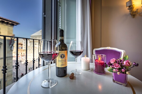 A table with two wine glasses, a bottle of wine, a candle, and a vase with flowers on a balcony overlooking a cityscape. - B&B La Terrazza sul Duomo (Florence)