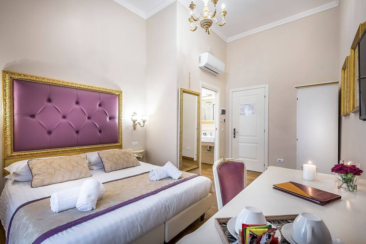A hotel room with a large bed, a bedside table with a book and a candle, and a view of the bathroom through an open door.