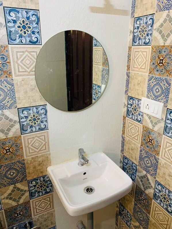 A bathroom with a white sink, a round mirror, and patterned tiles. - Mamata Courtyard Anjuna (Anjuna)