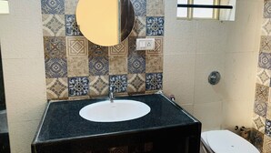 A bathroom with a sink, mirror, and toilet. The wall has patterned tiles. - Mamata Courtyard Anjuna (Anjuna)