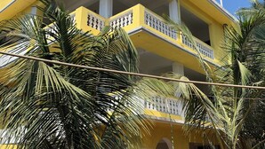 A multi-story yellow building with balconies, palm trees, and a staircase. - Mamata Courtyard Anjuna (Anjuna)