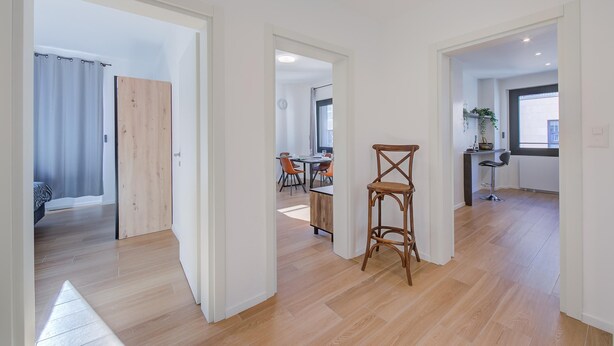 A spacious room with a wooden floor, a dining area with orange chairs, and a kitchen area with a bar stool. - Boutique Apartment 12 (Lugano)