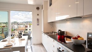 A modern kitchen with a large window, white cabinets, and a dining area with a table set for four. - Panoramic Penthouse in Lugano (Lugano)