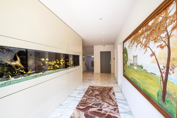A hallway with a long aquarium, a marble floor, and a large landscape painting on the wall.