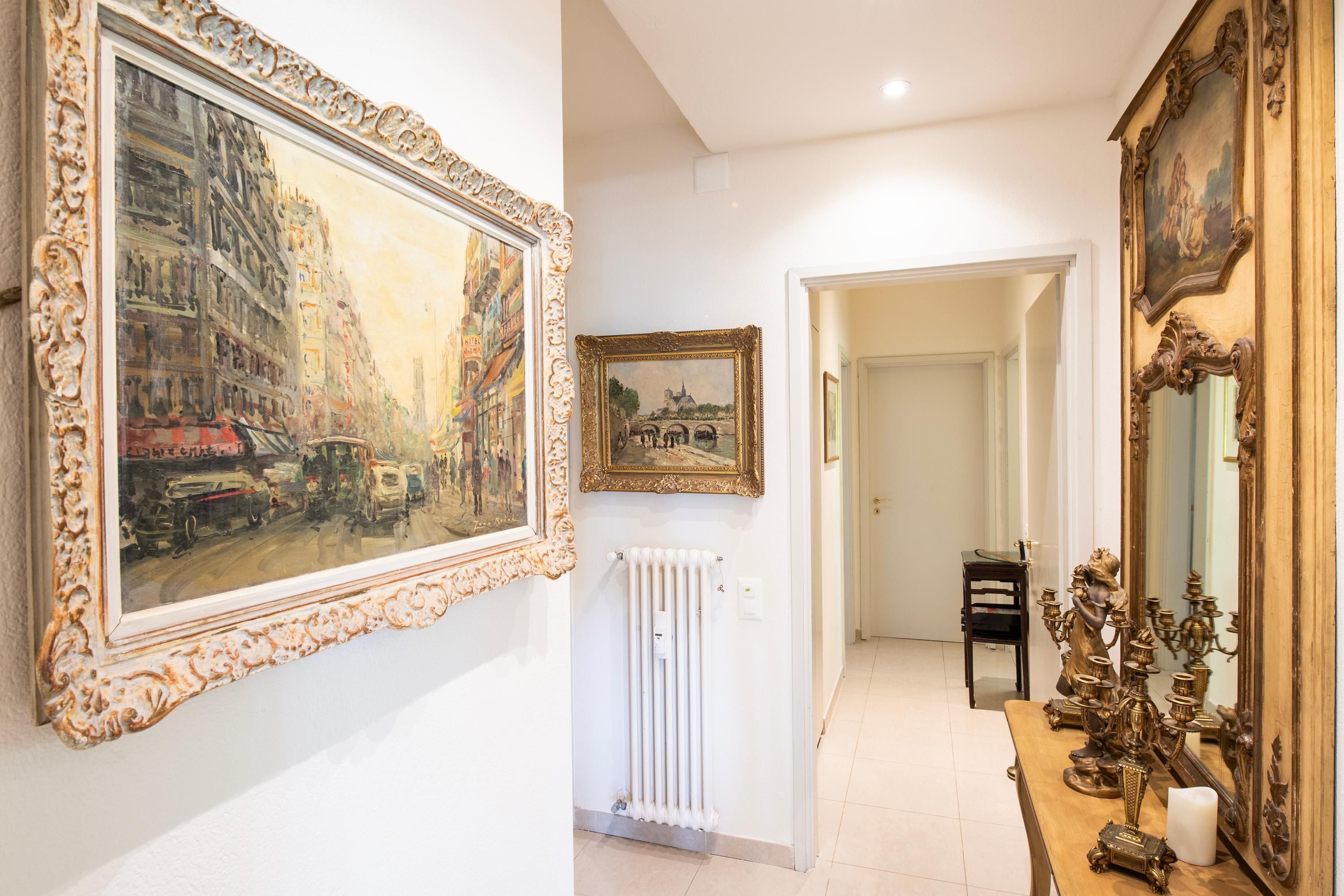 Un corridoio con dipinti decorativi, un termosifone e un tavolo con oggetti ornamentali.