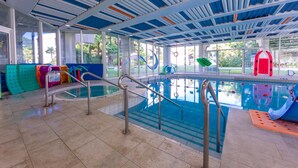 Una piscina interna con pareti in vetro trasparente, un soffitto blu e bianco e un pavimento piastrellato.