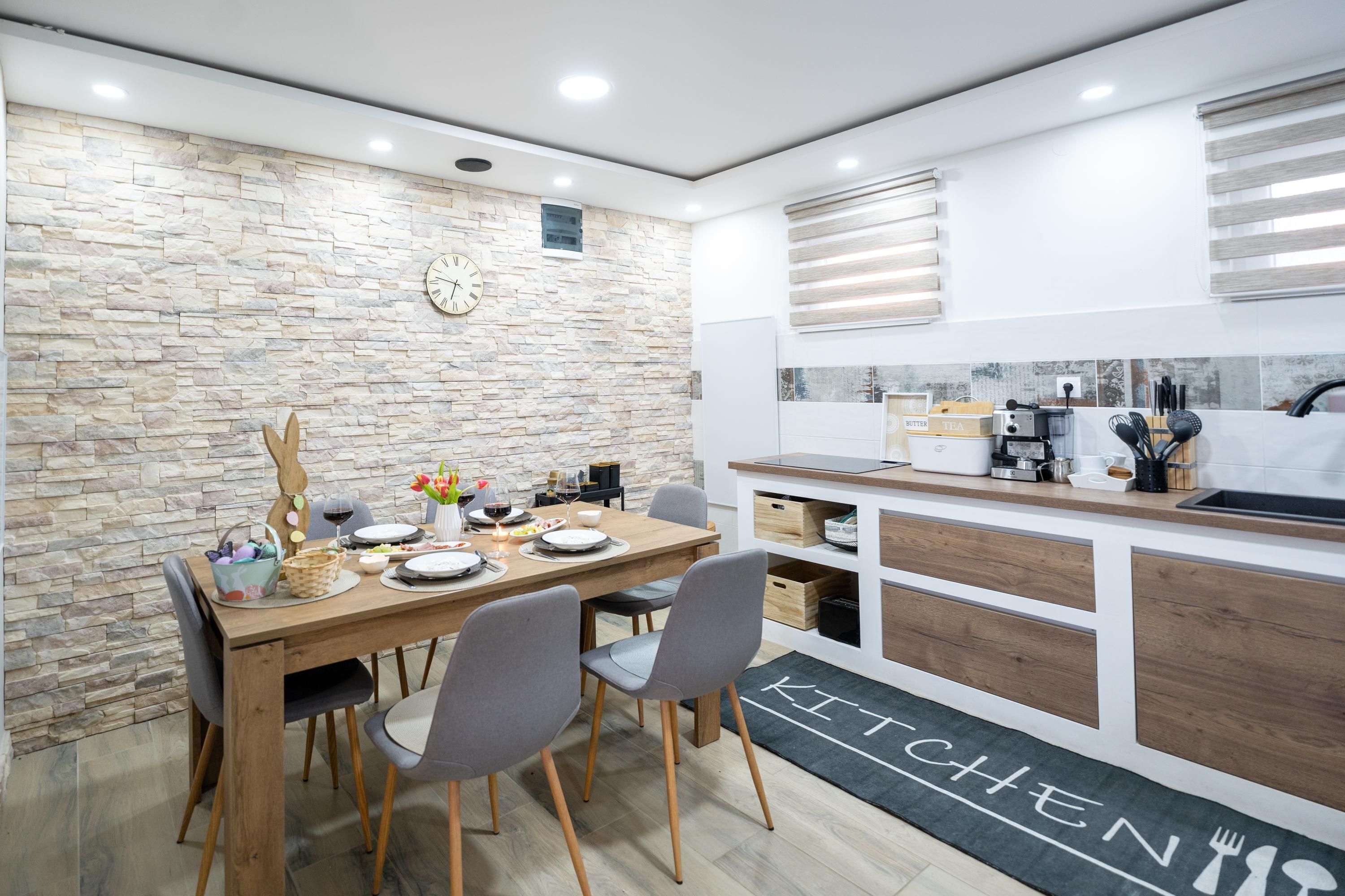 Une cuisine moderne avec un mur en pierre, des armoires en bois et un coin repas avec une table dressée pour quatre personnes.
