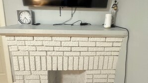 A flat-screen TV mounted on a wall above a white brick fireplace with a clock and a decorative item on the mantel. - Cozy house in welcoming Cleveland with AC, WiFi (Cleveland)