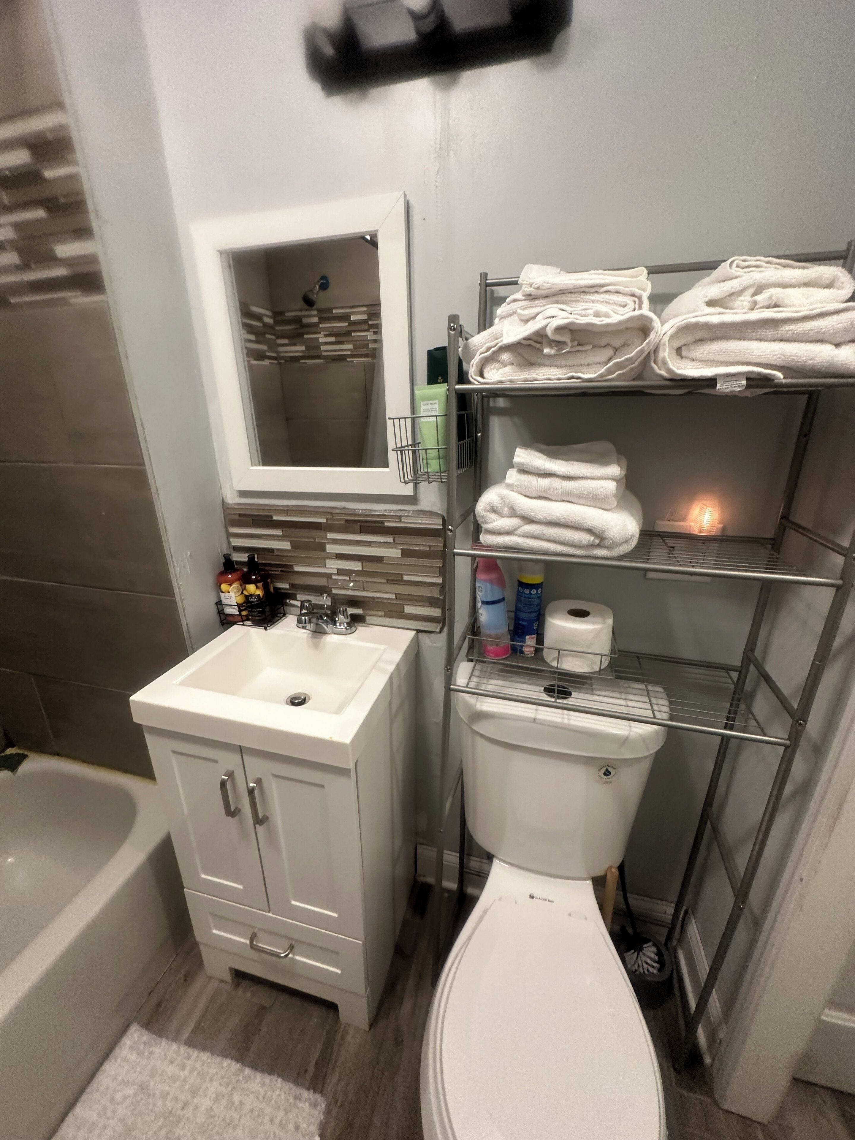 A bathroom with a white sink, mirror, and toilet. There are shelves with folded towels and toiletries.