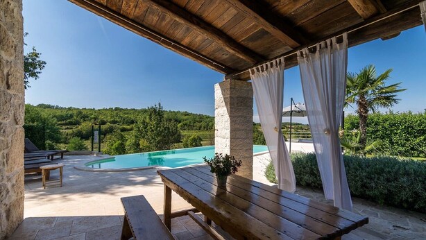 A covered outdoor area with a pool, stone benches, and a wooden table. - Villa Zvonar in Karojba (Karojba)