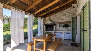 An outdoor kitchen area with a stone wall, wooden beams, and a table with benches. - Villa Zvonar in Karojba (Karojba)