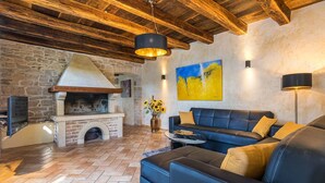 A cozy living area with a stone fireplace, a blue leather sofa, and a rustic wooden ceiling. - Villa Zvonar in Karojba (Karojba)