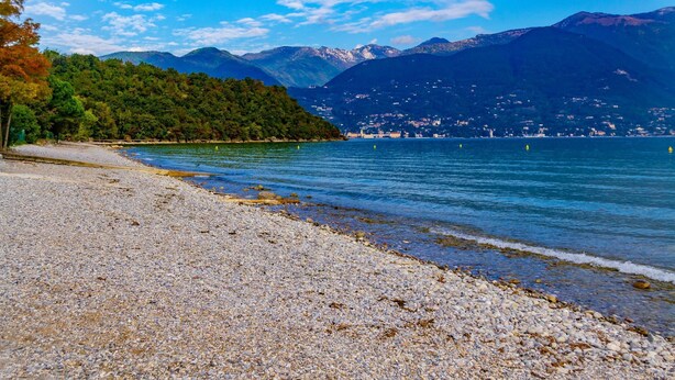 A pebble beach with clear water, mountains in the background, and a small town across the water. - Henry-historic Center 300mt From Lake (San Felice del Benaco)