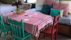A cozy dining area with a table set for two, a bench with cushions, and a view of greenery outside. - Moorestone- Back to Yesteryear (Guilderton)