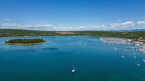 Luftaufnahme einer Küstenregion mit einem Yachthafen, Booten und einer kleinen Insel.