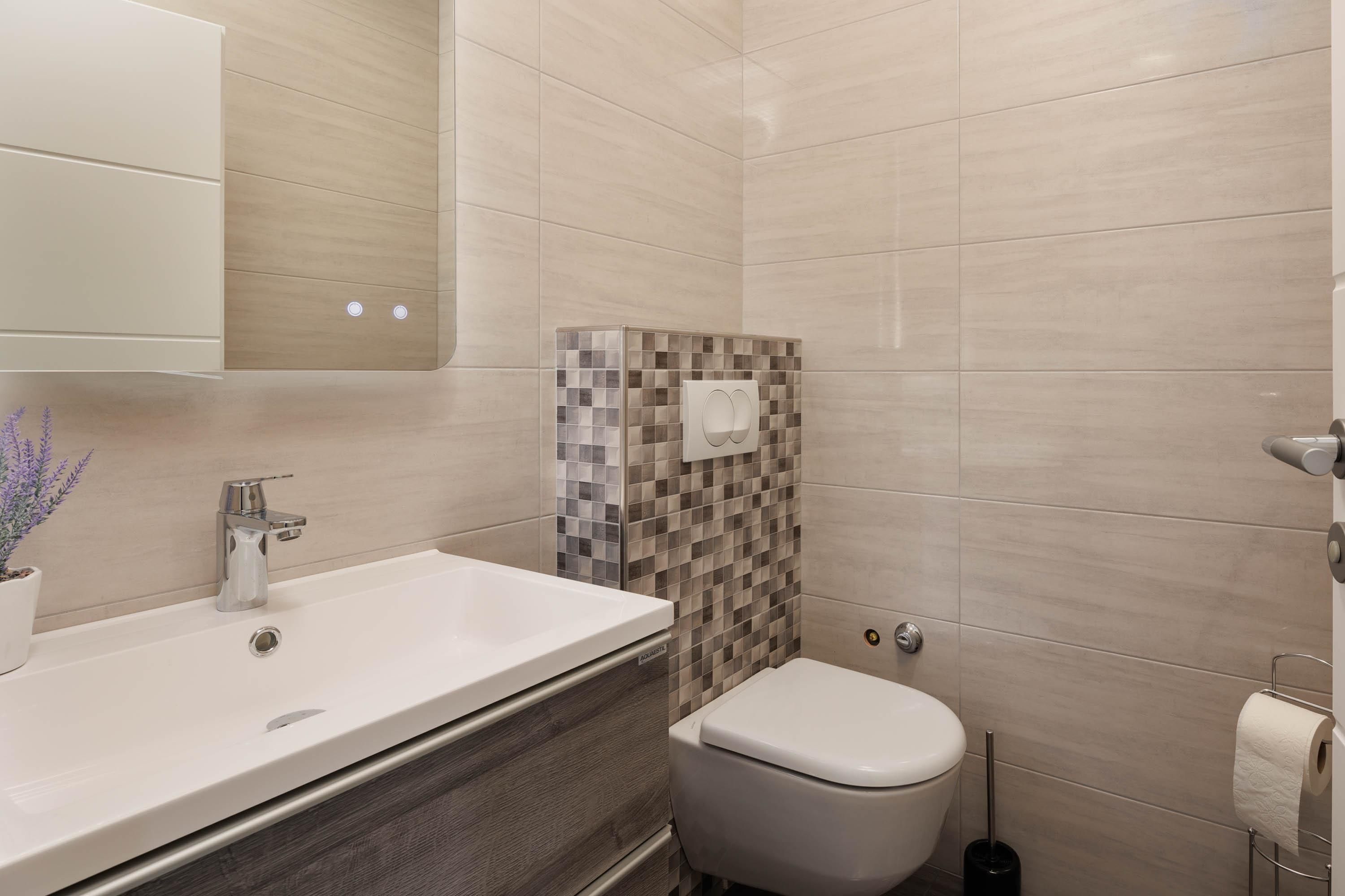 A bathroom with a white sink, a toilet, and a tiled wall.