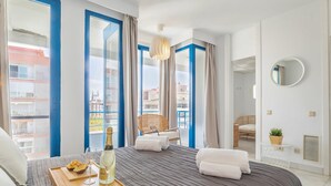 Une chambre d’hôtel avec un lit, un plateau avec une bouteille et un verre, une chaise et une vue sur l’extérieur.