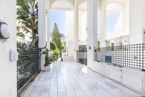 A corridor with white tiled flooring, black metal fencing, and a view of a building with columns and a staircase.