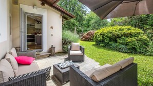 An outdoor patio with wicker furniture, a dining table with a tray of items, and a large umbrella.