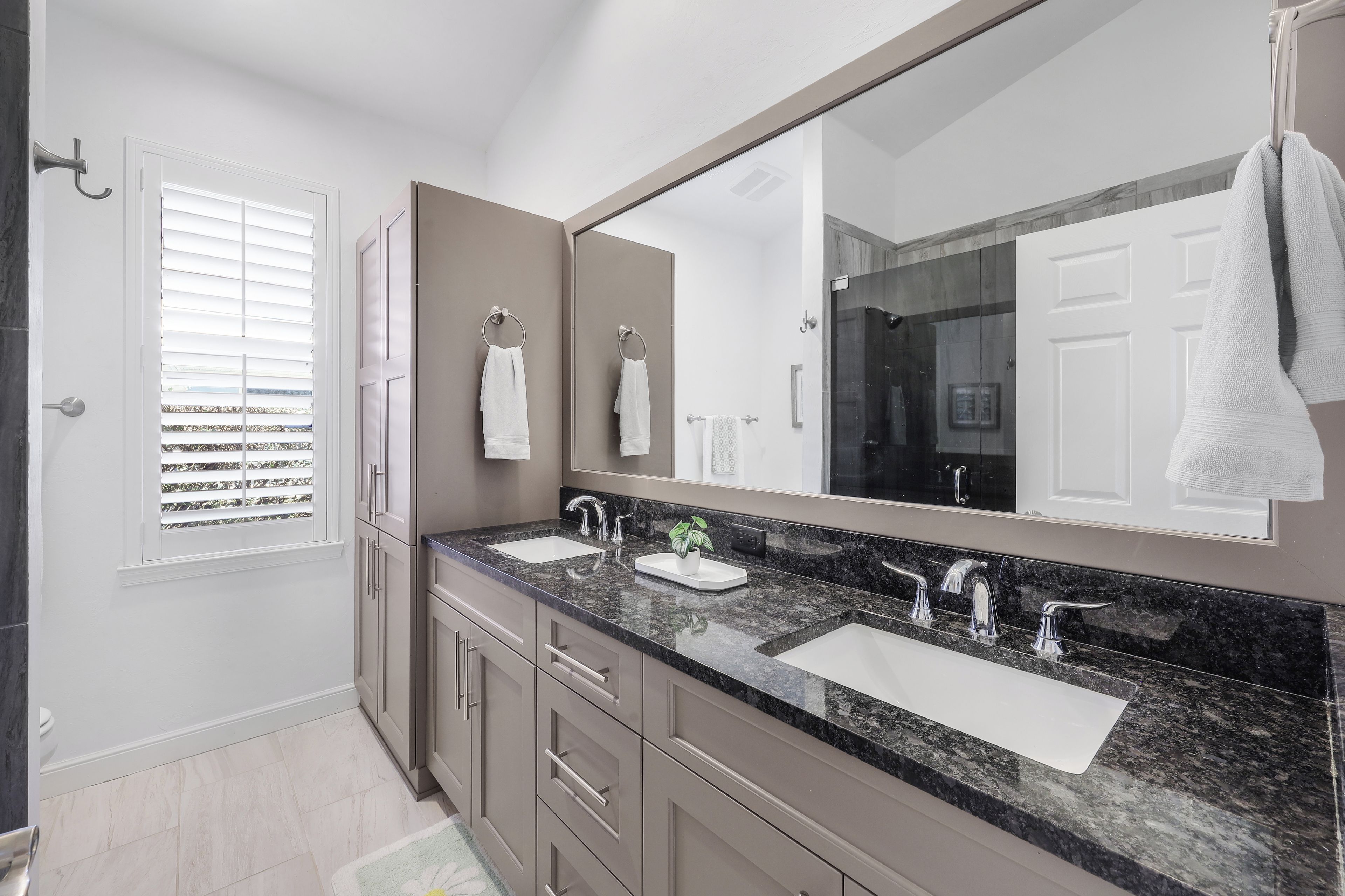 Un baño moderno con dos lavamanos, un espejo grande y una ventana con persianas.