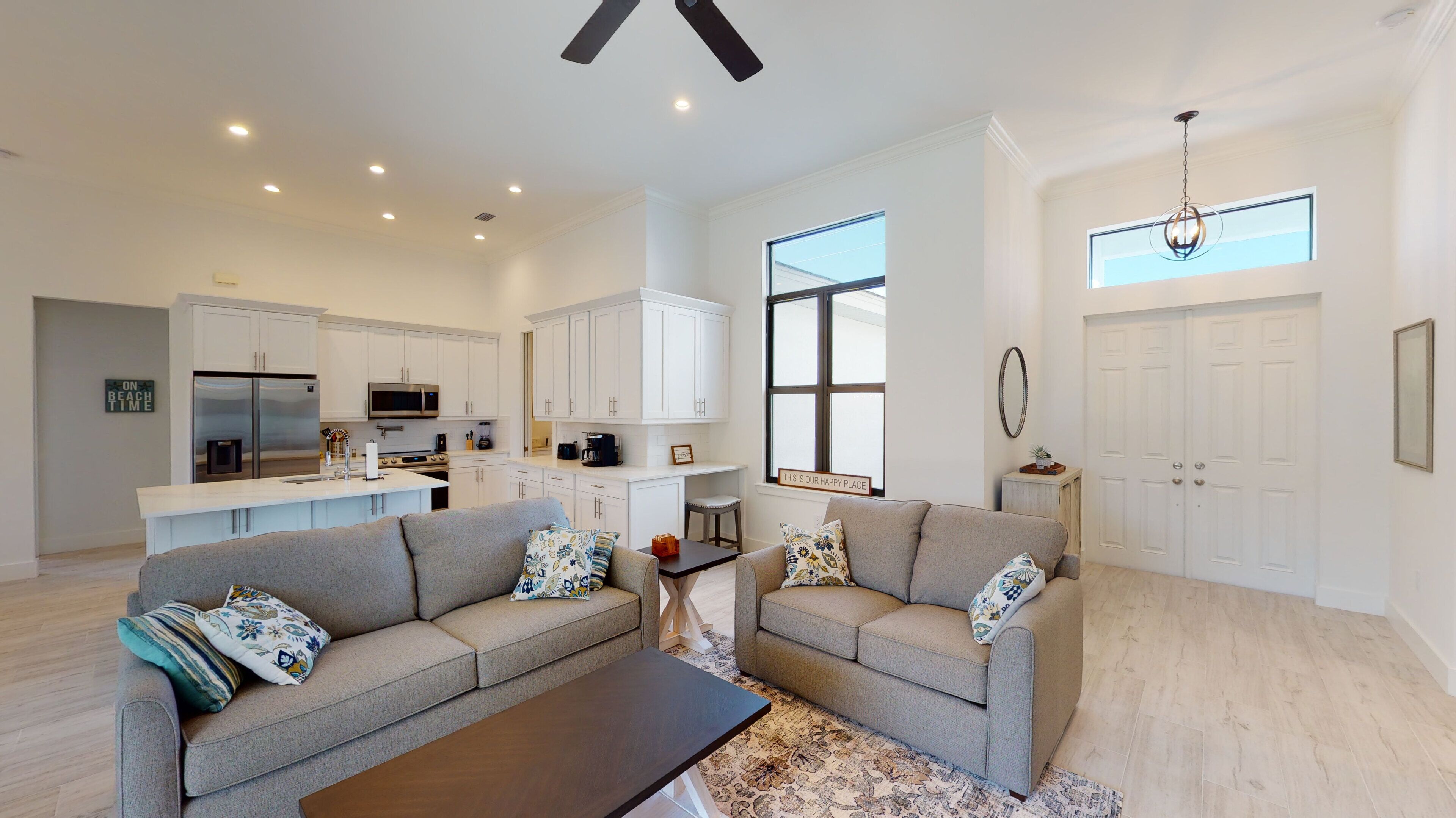 A spacious living room with two grey sofas, a coffee table, and a kitchen in the background.