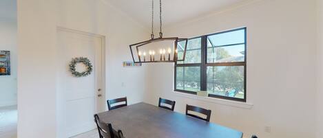 Une salle à manger avec une grande table, des chaises, un lustre, une fenêtre donnant sur un beau paysage et une porte ornée d’une guirlande.