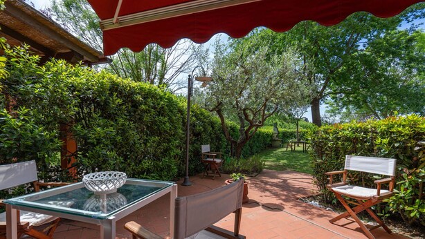 A patio with a glass table, cushioned chairs, and a red umbrella.