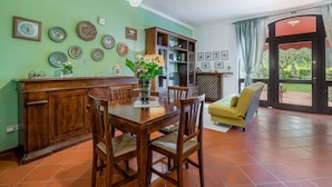 A dining area with a wooden table and chairs, a cabinet with decorative plates, and a sofa.