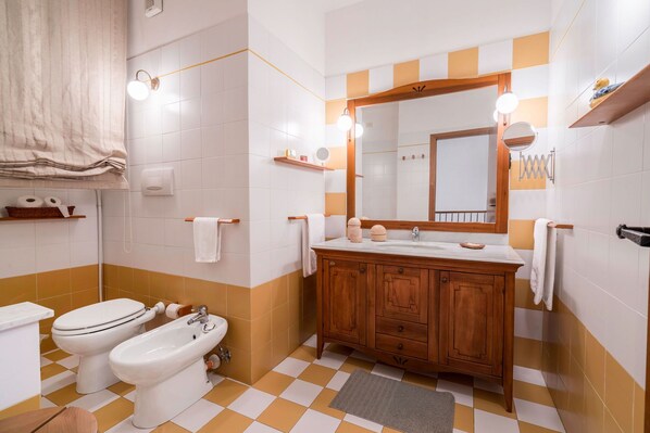 A bathroom with a wooden vanity, two sinks, a bidet, and a large mirror.