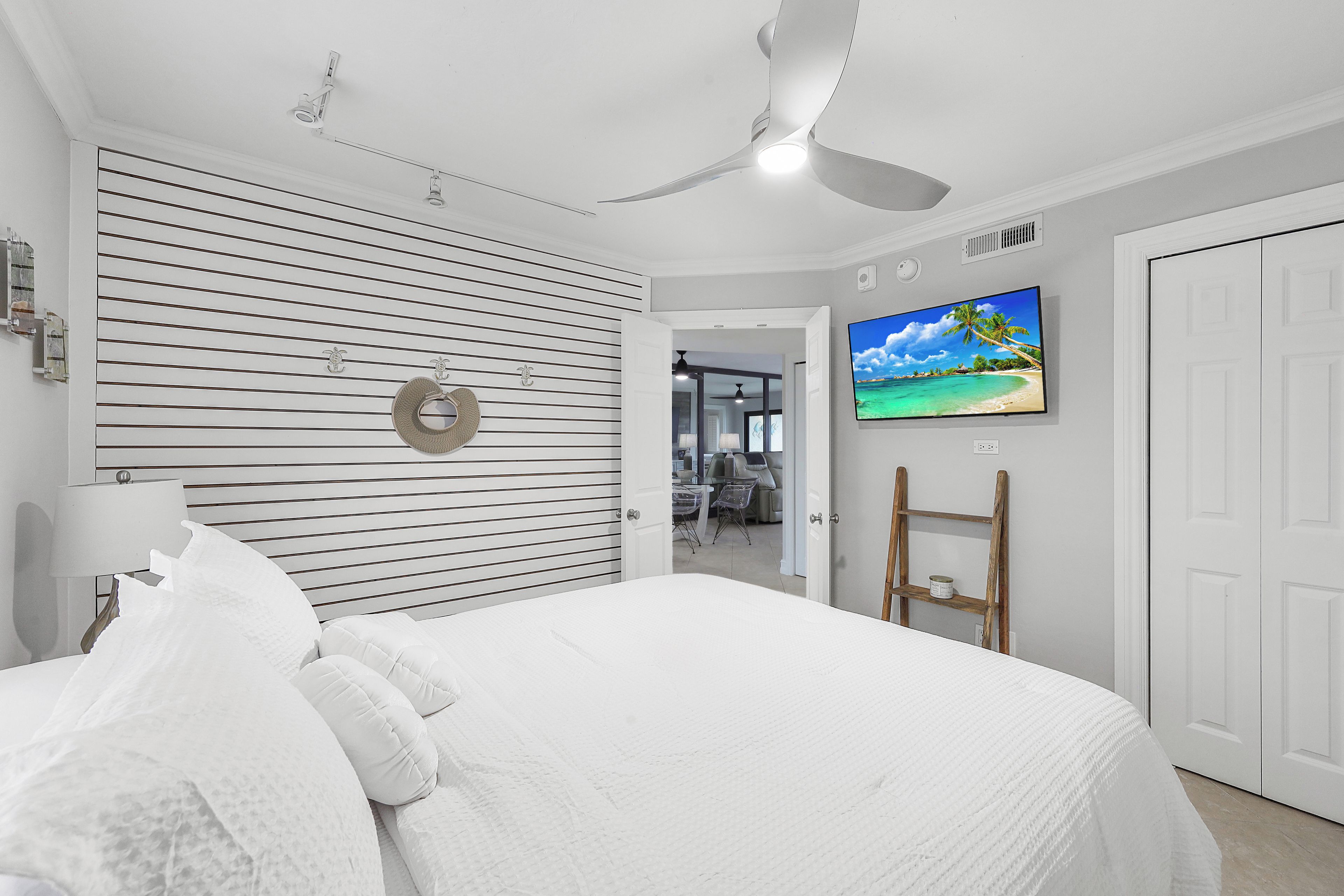 A bedroom with a bed, a ceiling fan, a TV on the wall, and a door.