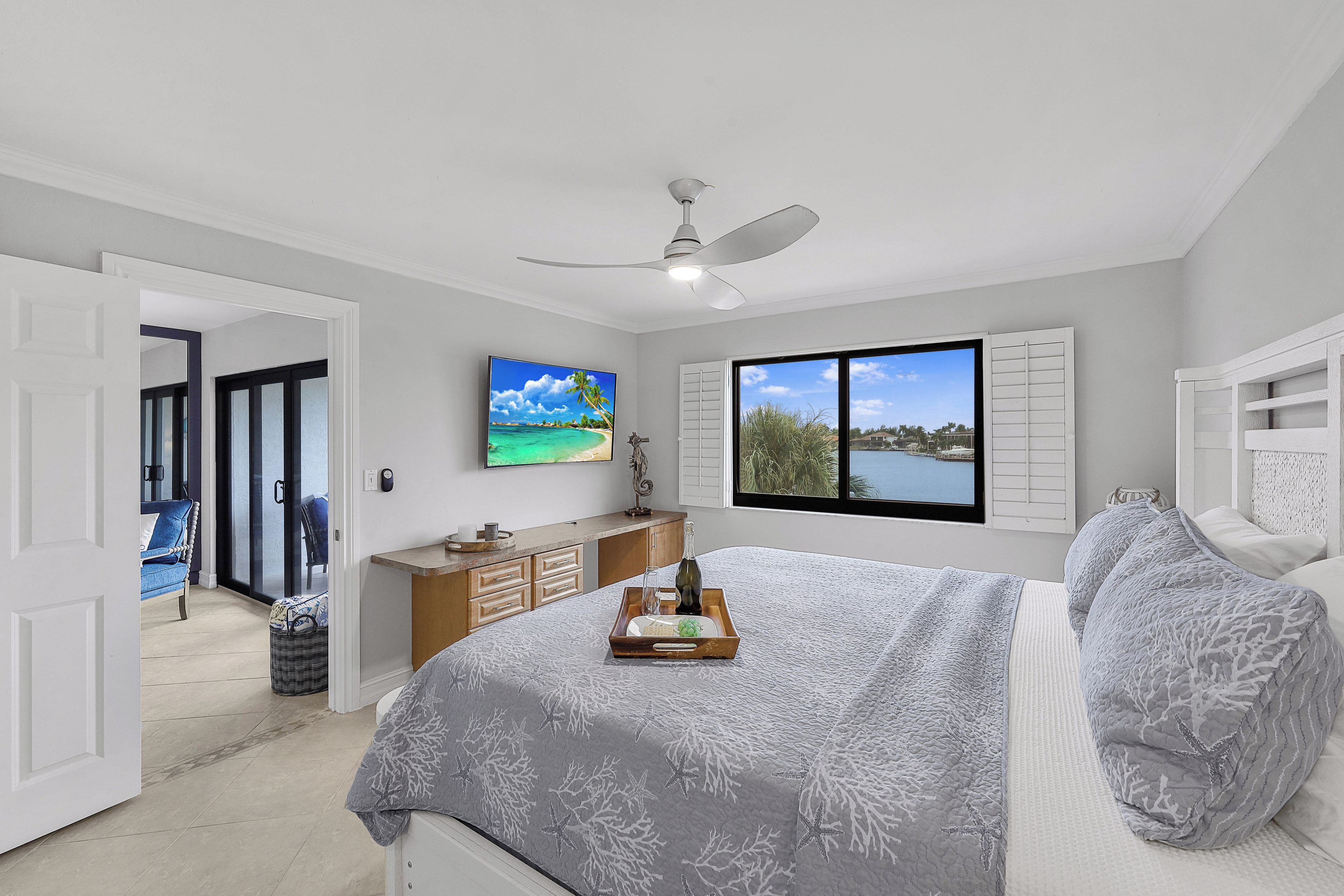 A bedroom with a bed, a TV, a window with shutters, and a view of the outdoors.