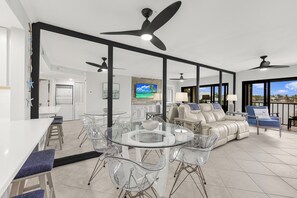 Un vaste espace de vie comprenant une table à manger en verre, des chaises transparentes, un canapé en cuir et un balcon avec vue.