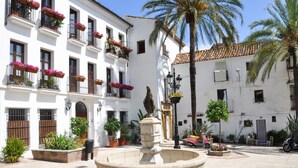 Une cour avec une fontaine, des bâtiments blancs dotés de balcons et des plantes en pot.
