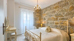 A bedroom with a stone wall, a bed with a metal headboard, a bedside table, and a chair. - Villa Lapis in Buzet (Buzet)