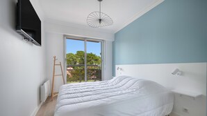 Un dormitorio con una cama grande, un televisor montado en la pared, un ventilador de techo y vistas al exterior mediante una puerta corrediza.