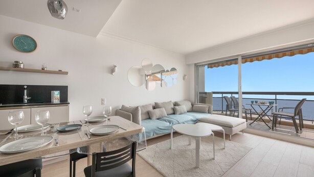 Una sala moderna con sofá, mesa de comedor y sillas. Cuenta con un balcón y vistas al mar.