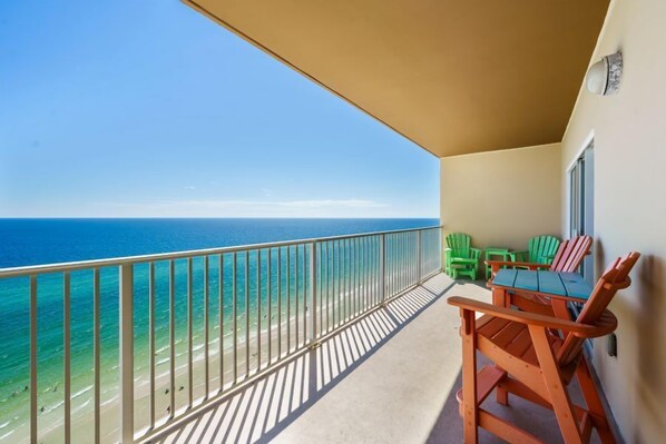 A balcony with a view of the ocean, a table with chairs, and a window.