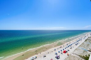 A beach with a clear view of the ocean and a sandy shore lined with umbrellas and beach chairs.