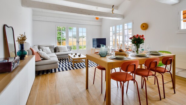 En moderne stue med sofa, sofabord og spiseområde med stole og et bord dækket til et måltid.