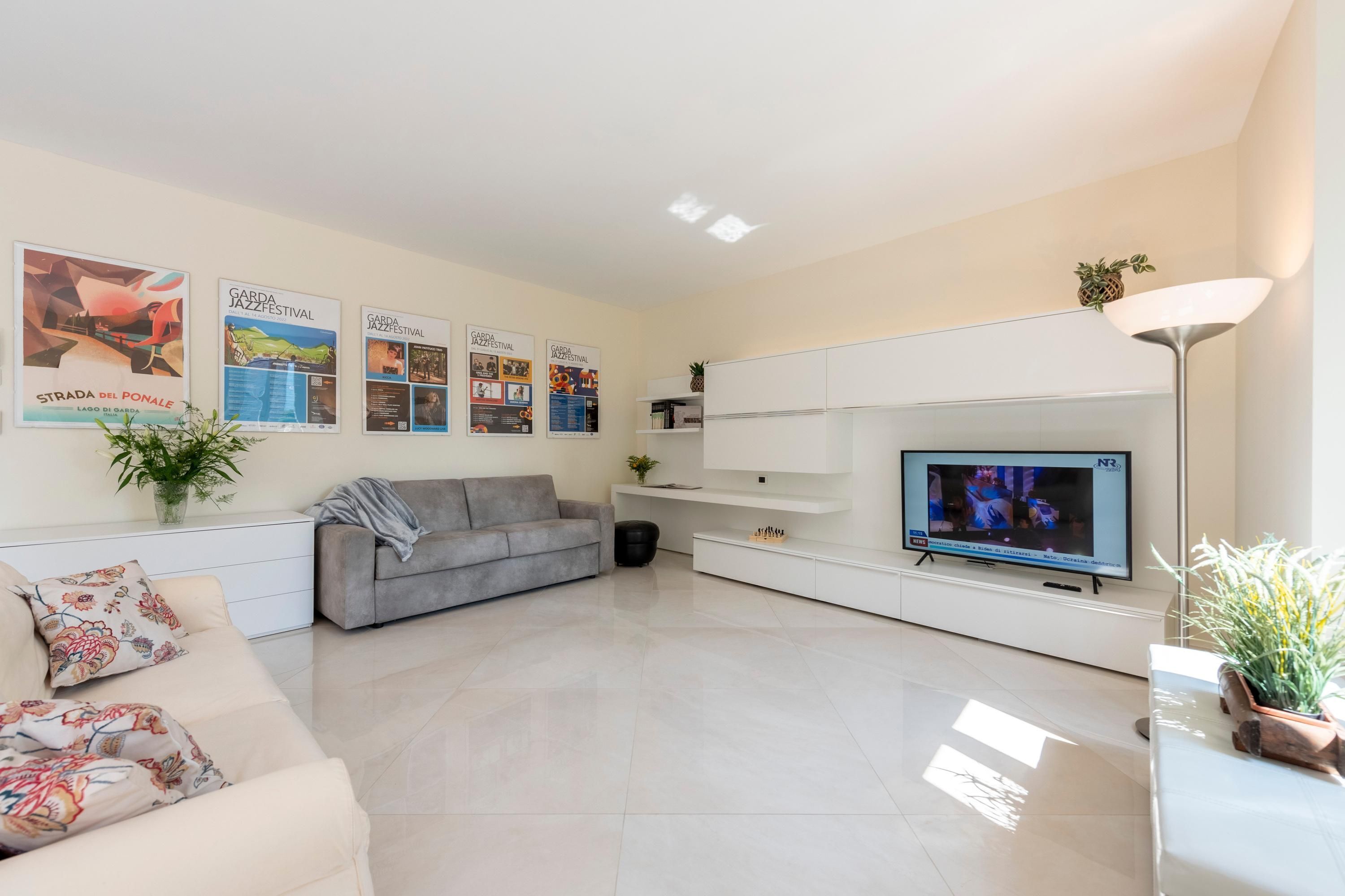 A modern living room with a grey sofa, a flat-screen TV, and a white entertainment unit.