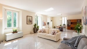 A spacious living room with a large window, a sofa, a coffee table, and a dining area with a table and chairs. - Life View Luxury Apartment (Riva del Garda)
