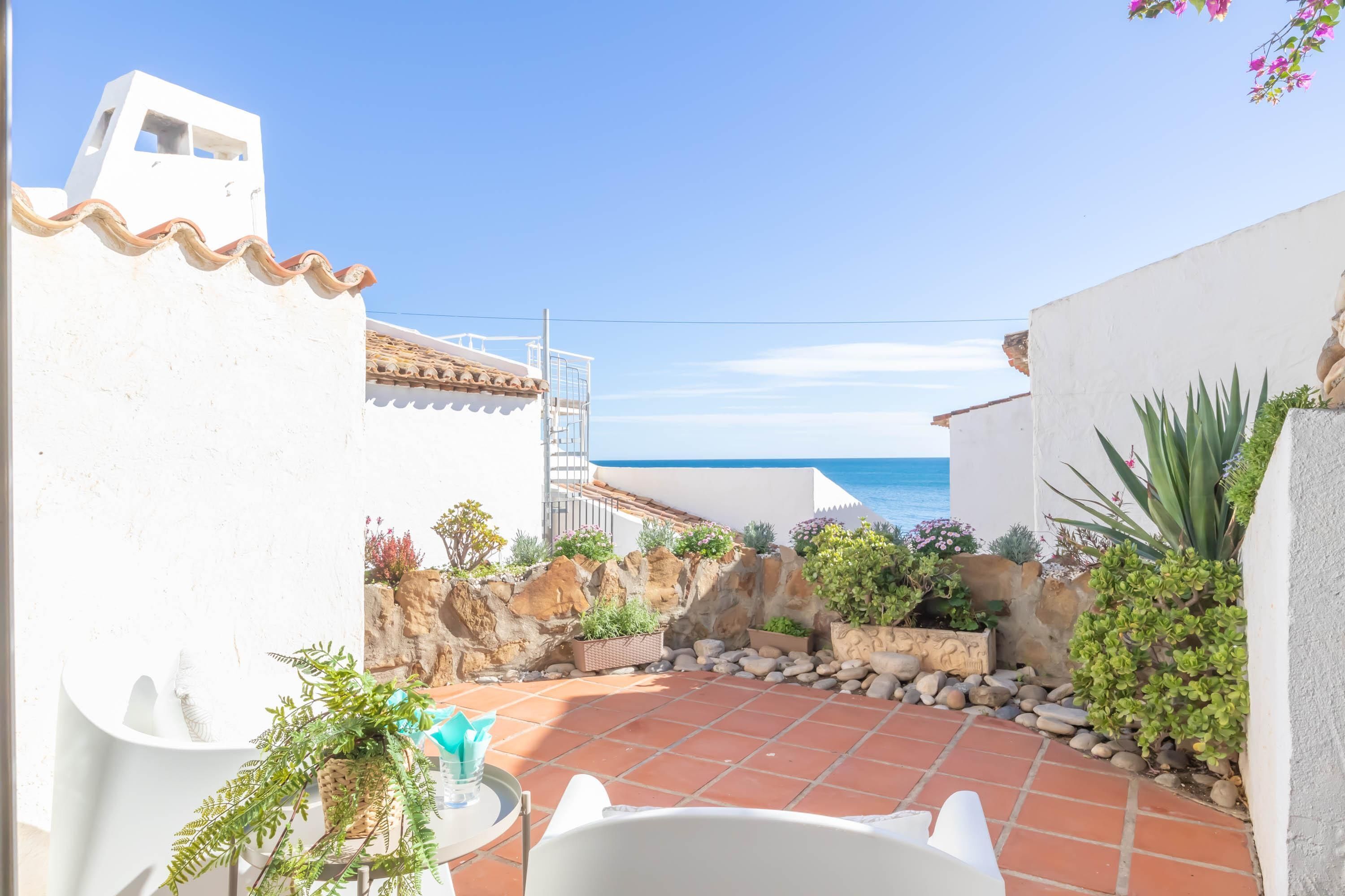 Eine Terrasse mit weißer Wand, gefliestem Boden und Blick auf das Meer.