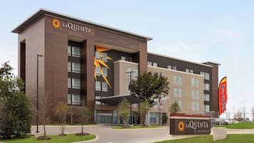 Ett La Quinta-hotell med en modern design, som kännetecknas av en tydlig sollogotyp och en välkomnande skylt.