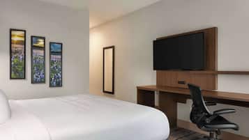 A hotel room with a large bed, a desk with a chair, a flat-screen TV, and three framed pictures on the wall.