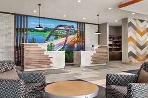 A reception area with a modern design, featuring a large digital screen displaying a scenic view, a staircase leading to a second floor, and a seating area with patterned sofas.