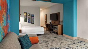 A hotel room with a bed, a desk with a computer, a TV, and a colorful abstract painting. - La Quinta Inn & Suites By Wyndham Austin South (Austin)