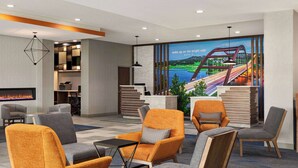 A hotel lobby with seating, a reception desk, a fireplace, and a mural of a bridge. - La Quinta Inn & Suites By Wyndham Austin South (Austin)