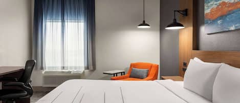Habitación de hotel con una cama grande, un escritorio, una silla de oficina, una mesita pequeña, una silla con cojín naranja y un cuadro en la pared.