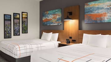 A hotel room with two beds, a wooden headboard, a nightstand, and three framed pictures on the wall.